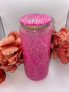 a jar with pink glitter on it next to flowers