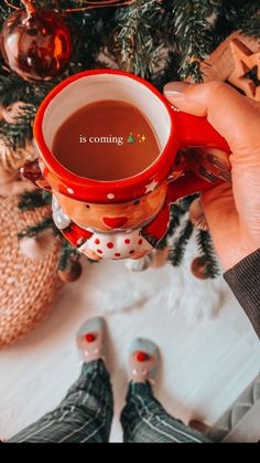 someone holding a coffee mug in front of a christmas tree