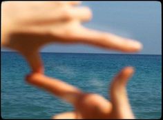 two hands in front of the ocean with a boat in the distance and one hand up to the camera