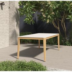 a table sitting on top of a wooden floor next to a tree and shrubbery