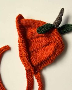 an orange knitted hat with a green leaf on the top and two small leaves attached to it