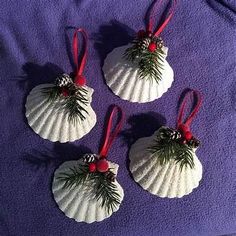 four seashell ornaments with pine cones and red bows on them sitting on a purple blanket