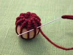 a red ball of yarn with a needle in it sitting on a green tablecloth