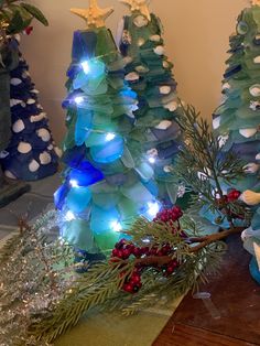 three christmas trees made out of plastic bottles and decorated with lights, are sitting on a table