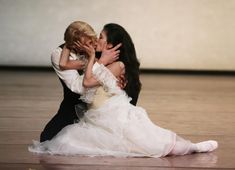 a woman in a white dress is kissing a man on the floor