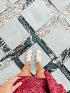 a woman's feet with white tennis shoes on standing in front of a tiled floor