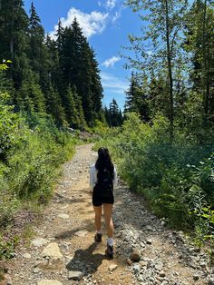 a woman walking down a dirt road in the woods on a sunny day with her back to the camera