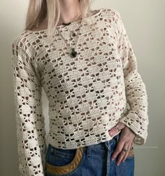 a woman wearing a crochet sweater and jeans with her hands in her pockets