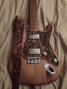 an intricately designed guitar is laying on a bed with a remote control in front of it