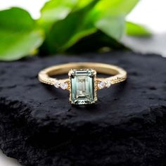 an emerald colored diamond ring sitting on top of a black rock