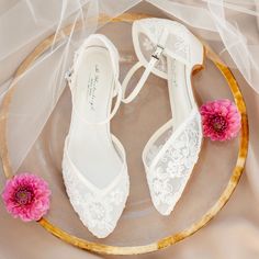 a pair of white shoes sitting on top of a glass plate next to a pink flower