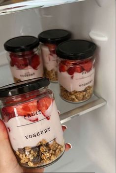 a person holding a jar filled with yogurt and strawberries in front of an open refrigerator