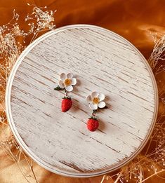 a pair of earrings with flowers and strawberries sitting on top of a wooden table