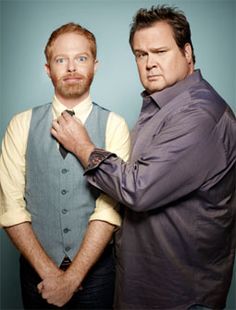 two men standing next to each other in front of a blue background with one man adjusting his tie