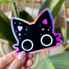 a hand holding up a sticker with a black cat design on it's face