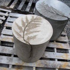 two cement vases sitting on top of pallets with leaves painted on the lids