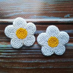 two white and yellow beaded flowers sitting on top of a wooden table