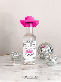 a bottle with a pink hat on top of it sitting next to disco ball decorations