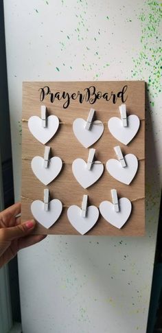 a person holding up a wooden plaque with white hearts on it and the words prayer board