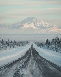 an empty road with snow on the ground and mountains in the background