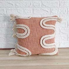 an orange pillow with white rope on the front and side, sitting against a brick wall