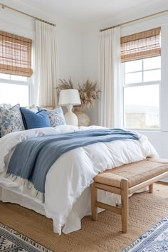 a bed with blue and white comforter in a bedroom next to two windows covered by drapes