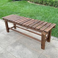 a wooden bench sitting on top of a cement floor next to a lush green field