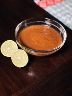 a glass bowl filled with sauce next to sliced limes on a wooden table top