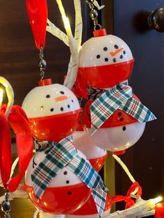 snowman ornaments hanging from a tree with red and white ribbons on them, in front of a door