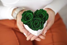 a woman holding a white box with three green roses in it's center and her hands