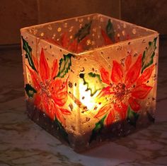 a lit candle holder with flowers painted on the inside and outside, sitting on a marble surface