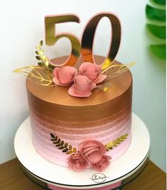 a pink and gold 50th birthday cake with flowers on the top is sitting on a table