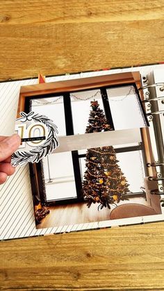 a hand holding a pair of scissors in front of a christmas tree inside an open binder