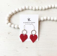 a pair of red beaded heart earrings sitting on top of a white necklace