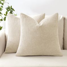 two pillows sitting on top of a white couch next to a potted green plant