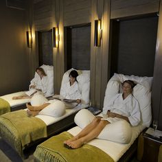 three women in robes are sitting on beds with pillows and blankets around them, reading books