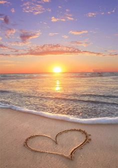 a heart drawn in the sand at sunset