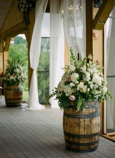 a wooden barrel filled with flowers sitting on top of a wooden floor next to windows