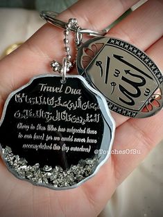 a hand holding a silver and black keychain with an islamic quote on it