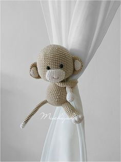 a crocheted stuffed monkey hanging from the side of a curtain with white drapes