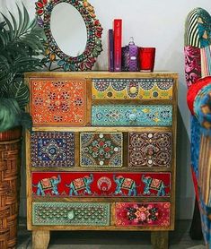 a multicolored chest of drawers sitting next to a potted plant and mirror