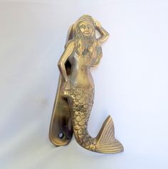 a gold colored mermaid bottle opener on a white background with the shape of a fish in it's mouth