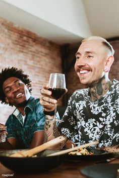 two men sitting at a table with wine glasses in their hands and food on the plate