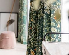 the curtains in this room are green and blue with flowers on them, along with a pink ottoman