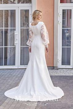 a woman in a white wedding dress standing on the sidewalk with her back to the camera