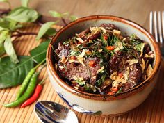 a bowl filled with meat and vegetables on top of a wooden table next to silverware