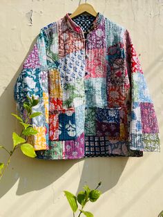 a colorful jacket hanging on a wall next to a green leafy plant in front of it