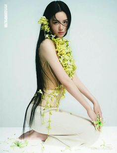 a woman with long black hair and flowers on her head is sitting in a white dress