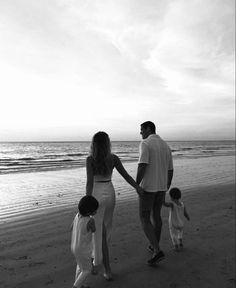 a man and woman holding hands while walking with two children on the beach at sunset