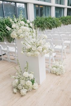 white flowers are in vases on the ground near rows of chairs with windows behind them